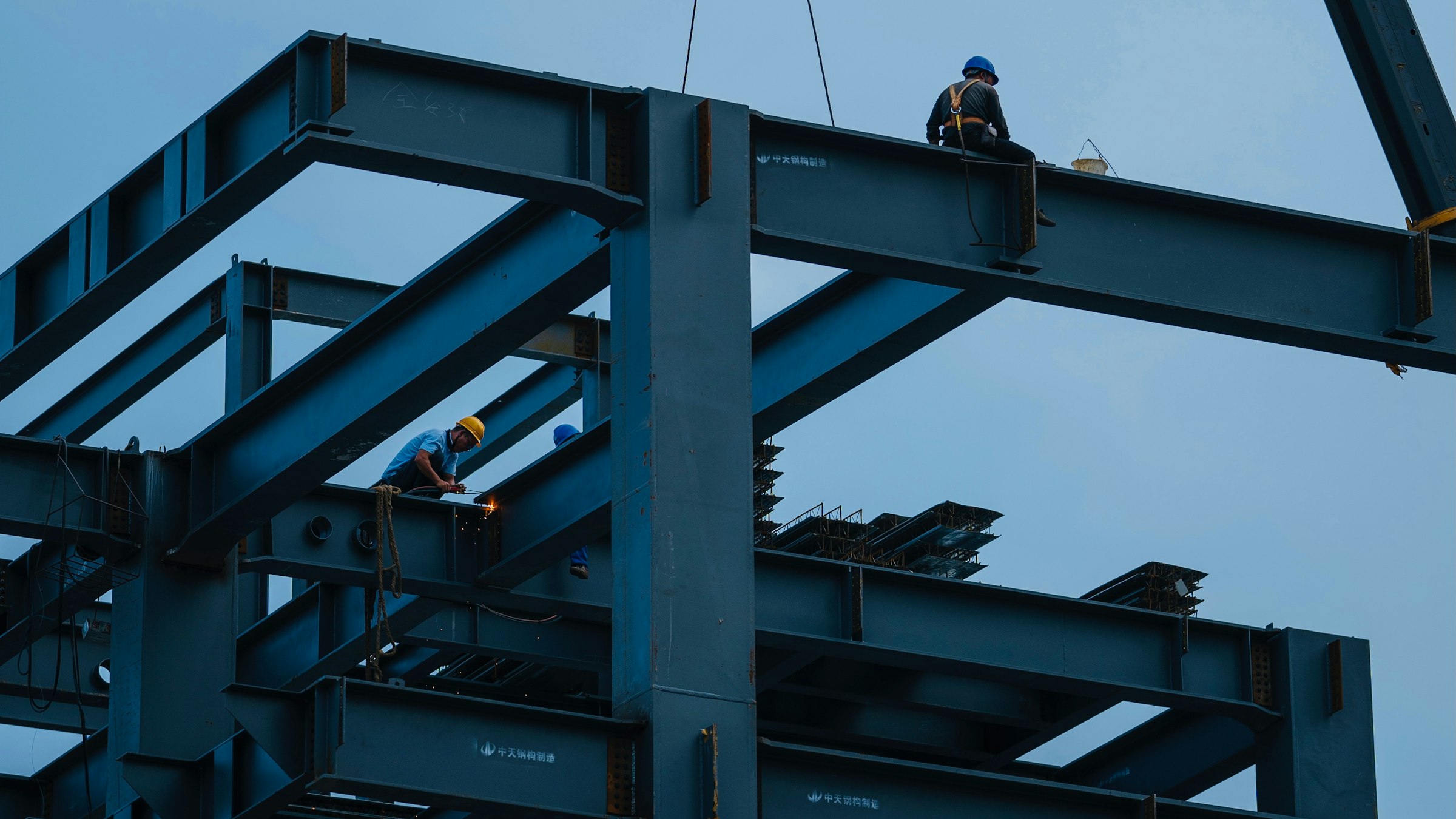 Construction workers assemble a steel structure with a crane